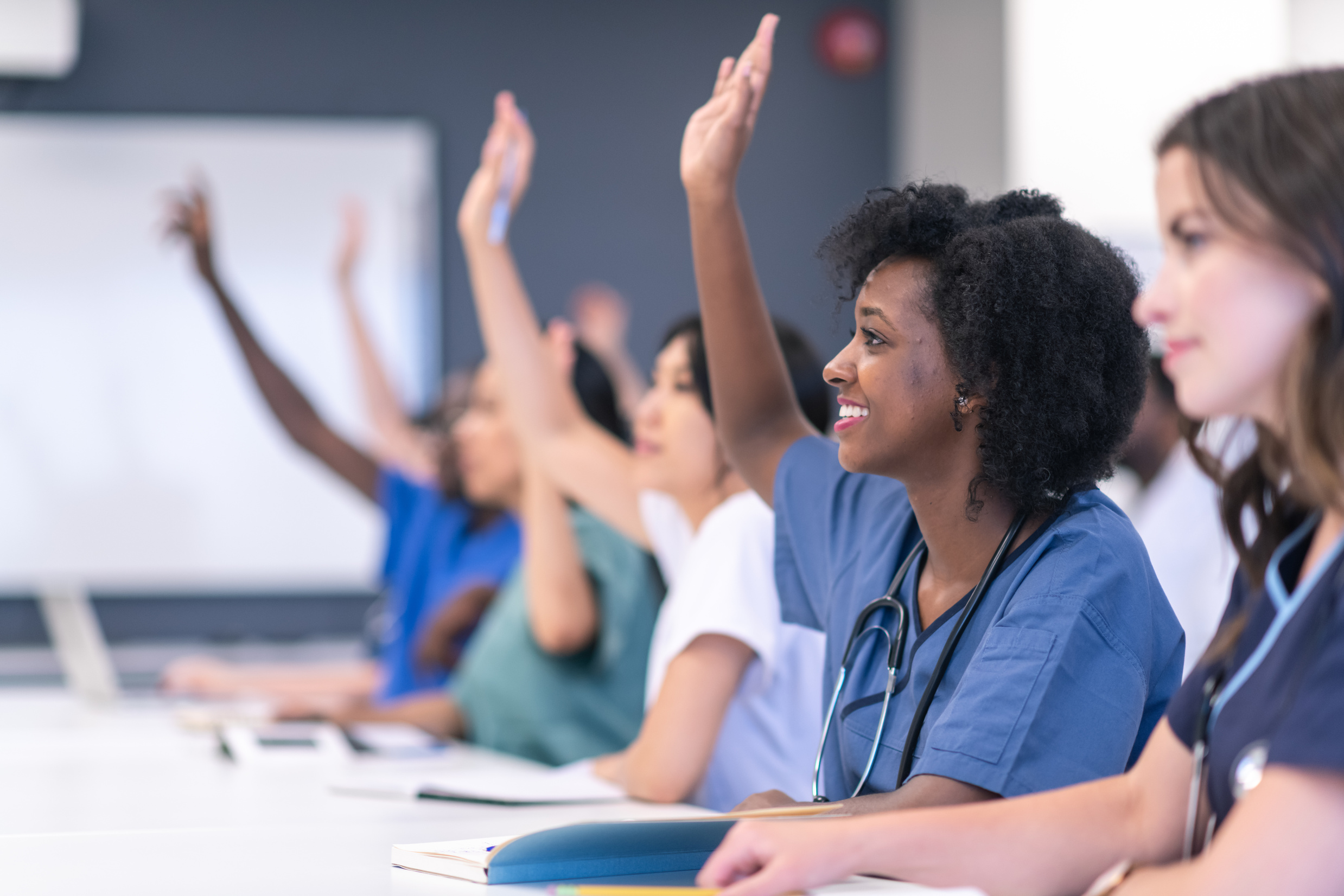 Students in medical training class raise hands in  lecture